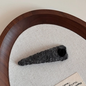 Detail of grey wool knit triangular hair clip showing textured fiber on canvas