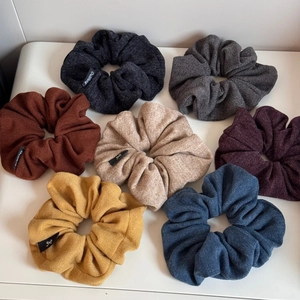 Close-up of seven textured knit scrunchies in assorted colors with small brand labels