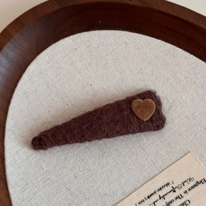 Detail of dark brown knitted hair clip with a light brown heart patch on a wooden tray