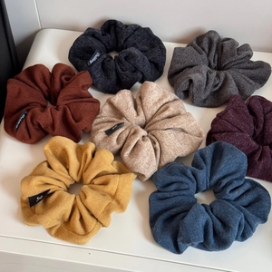 Close-up of seven large knitted scrunchies in varied colors on a white surface