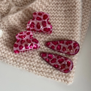 Detailed set of four pink leopard print acetate hair clips on a soft beige knit sweater