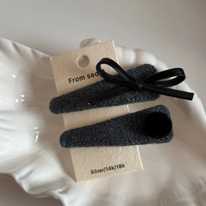 Detailed macro of dark grey tweed hair clips with leather bow on a white shell tray