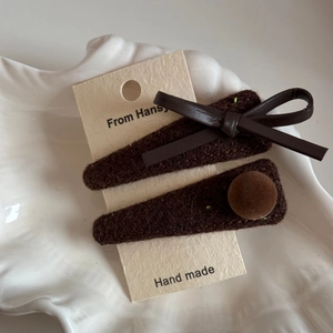 Close-up of brown velvet hair clips with leather bow and pom-pom detail on card
