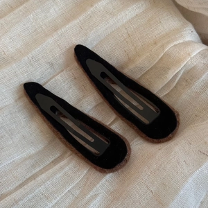 Detail view of two brown plush tear-drop hair clips on a soft beige textured fabric