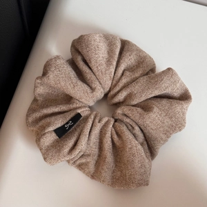 Macro shot of knitted oversized scrunchie in beige featuring a black bow tag detail
