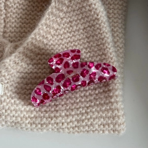 Macro detail of pink leopard acetate hair claw clip on beige knitted fabric