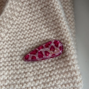 Detailed close-up of a pink leopard print acetate hair claw clip on a beige knit background
