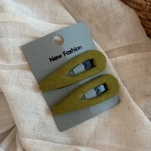 Close-up of olive green knitted BB hair clips set on a card with neutral fabric background