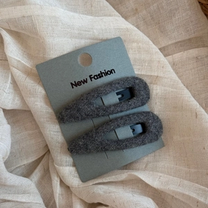 Detail of two dark gray wool felt snap hair clips on a New Fashion display card