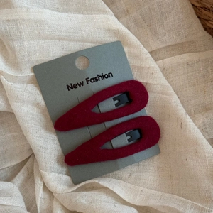 Detail view of burgundy plush teardrop BB hair clips on a gray card over fabric