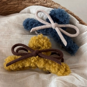 Detail view of plush bow claw clips with curly faux fur texture in yellow and blue
