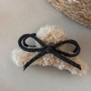 Detail shot of beige plush hair claw clip with dark grey bow accent for winter