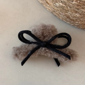 Detailed close-up of brown plush hair claw clip with black ribbon bow on stone surface