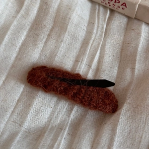 Close-up of rust brown knitted hair clip with soft textured wool and black metal base
