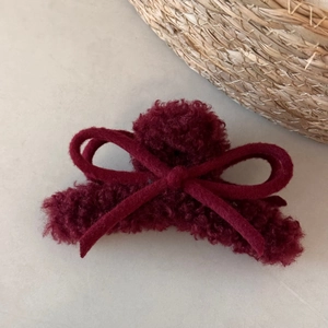 Close-up of fluffy burgundy plush hair claw clip with a ribbon bow on a beige background