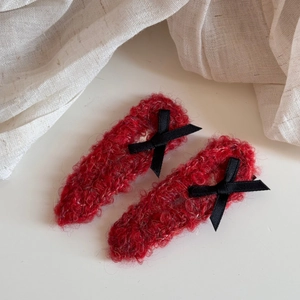 Close-up of red plush hair clips with black satin bows on a soft white background