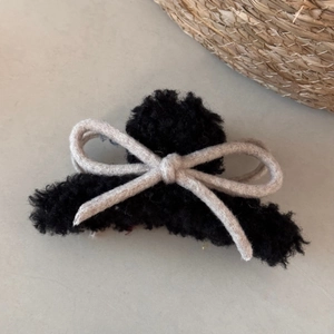 Detail of black faux lamb wool hair claw with a minimalist woven beige bow tie accessory