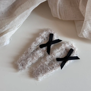 Detailed macro view of soft beige plush bow hair clips with black silk ribbons