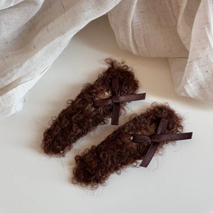 Detail view of coffee-colored faux shearling hair clips with elegant brown silk bows