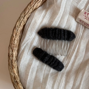 Detailed macro view of black knitted hair comb and clip set on white cotton fabric