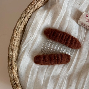 Close-up of brown knitted hair combs with soft wool texture and silver metal teeth