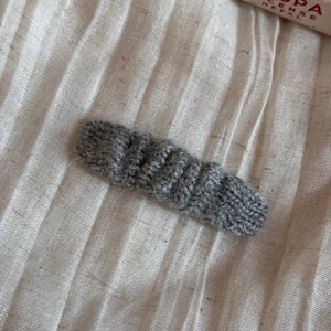 Close-up of grey knitted hair clip with warm wool texture and woven pattern on linen