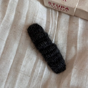 Close-up of black knitted wool hair clip with a vintage texture on beige fabric