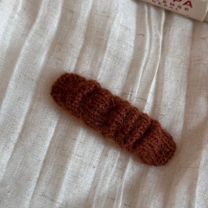 Detail shot of a dark brown knitted hair clip with rich texture on cream fabric