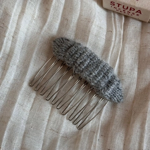 Detailed close-up of a grey knitted hair comb showing the soft wool texture and metal teeth
