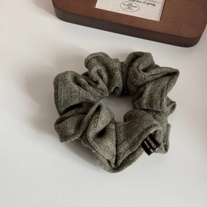 Close-up of dark green knitted scrunchie with handmade woven label on a wooden tray