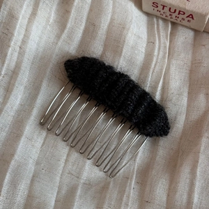 Detailed close-up of a black knitted hair comb with metal teeth on a rustic linen background