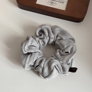 Detailed view of light grey knitted scrunchie with textured fabric and small woven label