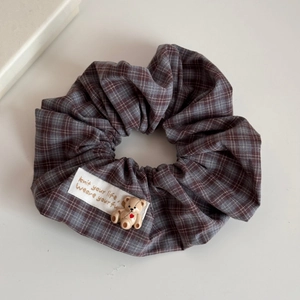 Detailed close-up of brown checkered scrunchie with cute 3D bear and textile label tag
