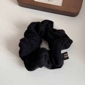 Detail view of black knitted scrunchie with Made in Korea tag on a white table