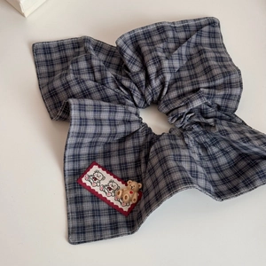 Detail view of plaid bow scrunchie with cute brown teddy bear ornament and fabric texture