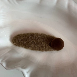 Détail de la barrette ovale en polaire marron avec perle décorative sur plateau blanc