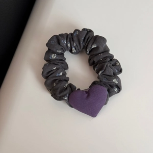 Detail view of dark grey floral hair scrunchie with a purple heart-shaped ornament
