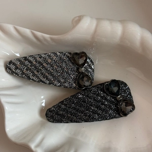 Detail of dark grey tweed water-drop hair clips with heart-shaped gems in a shell tray