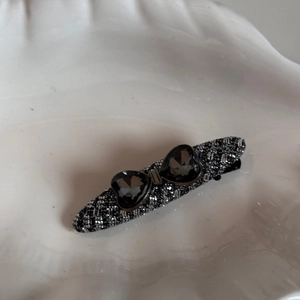 Detail of tweed wrapped hair clip featuring two dark grey heart-shaped rhinestones