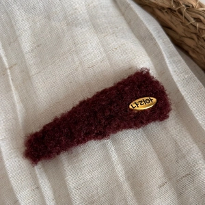 Détail de la pince à cheveux en peluche bordeaux avec étiquette ovale dorée