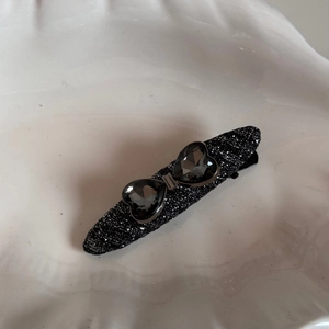 Detail of black glitter hair clip with grey crystal hearts forming a bow design