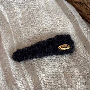 Vue détaillée d'une pince à cheveux triangulaire en peluche noire avec plaque dorée