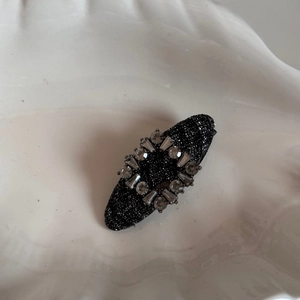 Close-up of black glitter hair clip with rectangular rhinestone frame on wavy background
