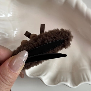 Detailed view of brown plush hair clip with ribbed ribbon and buttons on ceramic tray