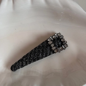 Detailed close-up of a sparkling black fabric hair clip with luxury rhinestone rectangle decor
