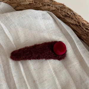 Détail macro d'une pince à cheveux en peluche bordeaux avec boule de velours chic