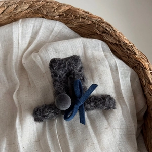 Dettaglio di fermaglio in maglia grigia con fiocco in velluto blu e pompon di peluche
