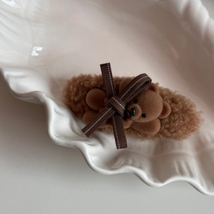Close-up of a brown plush hair clip with a teddy bear and ribbon bow on a white plate