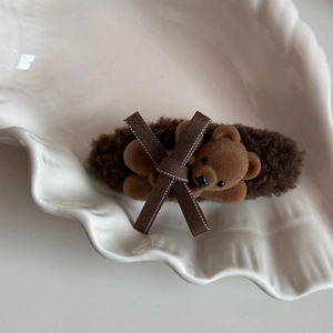 Detail of plush brown teddy bear hair clip with velvet bow on a ceramic shell dish