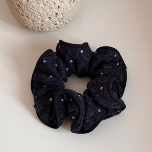 Close-up of a dark grey polka dot knit scrunchie with soft ruffled edges and texture